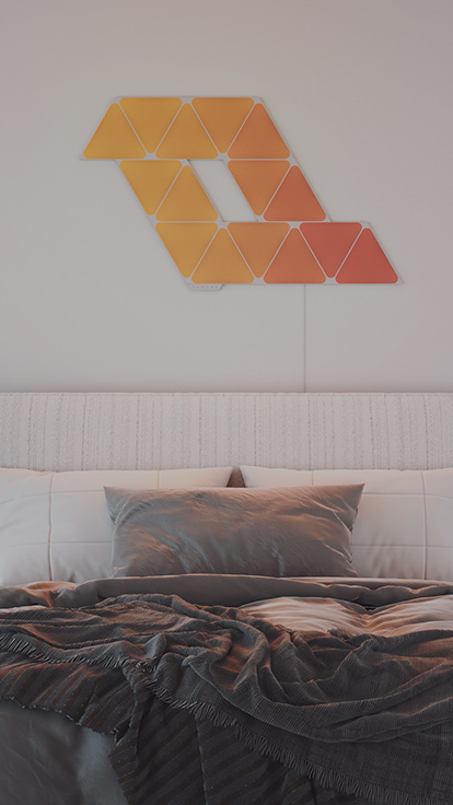 침대 위 벽면의 Nanoleaf Shapes Triangles 15 패널 레이아웃 이미지입니다. 이 스마트 라이트 패널은 침실 조명과 이상적인 분위기 연출에 완벽합니다.