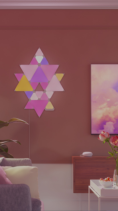 거실 TV 옆 벽면에 Nanoleaf Shapes Triangle 및 Mini Triangle 레이아웃을 연출한 이미지입니다. RGB 라이트 패널은 링커로 서로 연결되어 고유한 디자인을 만들어 낼 수 있습니다.