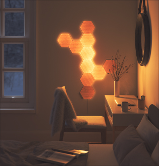 Đây là hình ảnh bố cục thiết kế 10 ô đèn Nanoleaf Elements được gắn trên tường cạnh bàn trong phòng ngủ. Ô đèn thông minh dạng mô-đun được gắn chặt vào tường bằng keo dính đi kèm và kết nối với nhau bằng khớp nối. Ô đèn hình lục giác vân gỗ là sản phẩm trang trí lý tưởng giúp phòng ngủ thêm phong cách và cá tính, đồng thời có thể thay đổi ánh sáng theo ý bạn.
