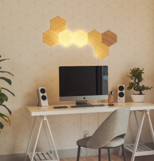 This is an image of a 7 panel layout of Nanoleaf Elements Wood Look Hexagons mounted on the wall above a computer. These modular smart light panels create a unique design and illuminate your space with a natural glow. The perfect lights to fill your personal office with.
