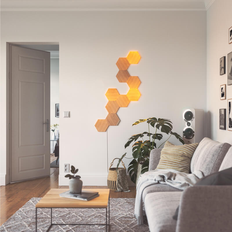 Ô đèn thông minh dạng mô-đun hình lục giác vân gỗ Nanoleaf Elements Thread-enabled được gắn lên tường trong phòng khách. HomeKit, Google Assistant, Amazon Alexa, IFTTT. 