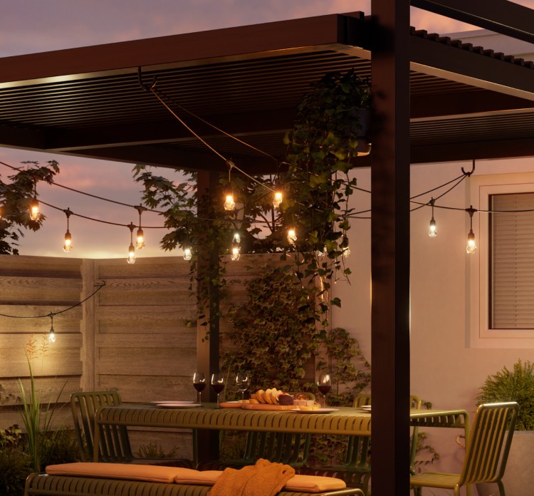 Spacious outdoor patio with wooden flooring, surrounded by lush greenery. Four glasses of wine on the table illuminated by smart outdoor string lights. Wooden fence adorned with additional LED string lights