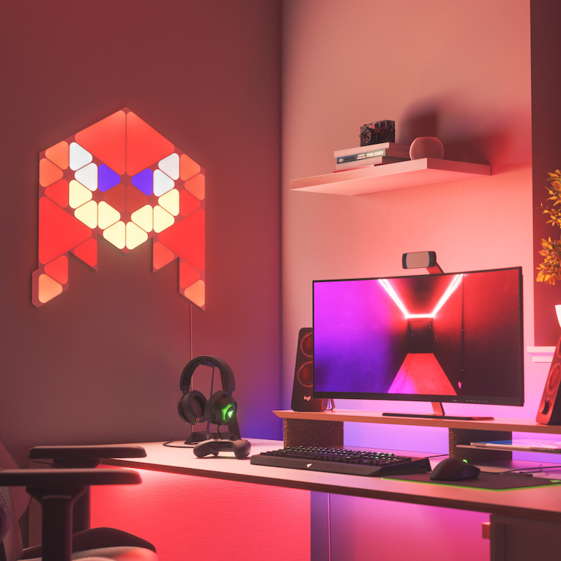 Nanoleaf Shapes Thread enabled color changing triangle and mini triangle smart modular light panels mounted to a wall above a battlestation as Knuckles. Sonic the Hedgehog 2. Tương tự với Philips Hue, Lifx. HomeKit, Trợ lý Google, Amazon Alexa, IFTTT.
