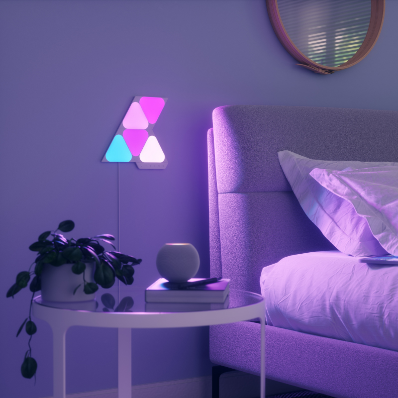 Ô đèn thông minh dạng mô-đun hình tam giác nhỏ có thể thay đổi màu sắc Nanoleaf Shapes Thread-enabled được gắn lên tường trong phòng ngủ. Tương tự với Philips Hue, Lifx. HomeKit, Trợ lý Google, Amazon Alexa, IFTTT.
